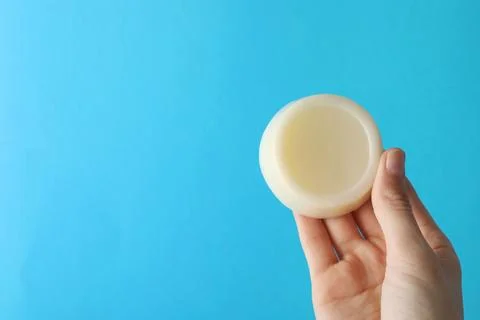 Woman holding solid shampoo bar against light blue background, closeup. Spa.. Foto stock