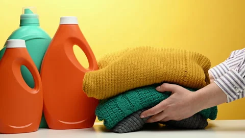 Woman holding a stack of knitted folded sweaters on a yellow background. Washing Stock Footage 165952544