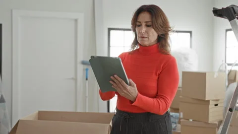 Woman holding tablet with both hands while organizing moving boxes in build.. Video stock 337441898