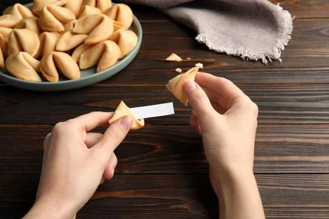 Woman holding tasty fortune cookie and paper with prediction at wooden table, Stock Photos