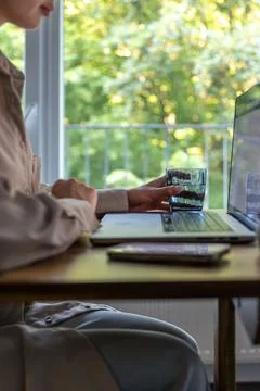 Woman holding water while using laptop. Remote work at a home desk. 스톡 사진