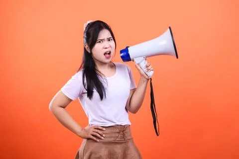 Woman holding white megaphone on solid bright orange background with dark hai Stock Photos