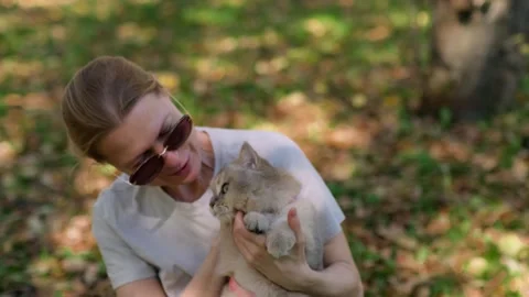 Woman holds cat gently while sitting under trees shade. Stock Footage 336909857