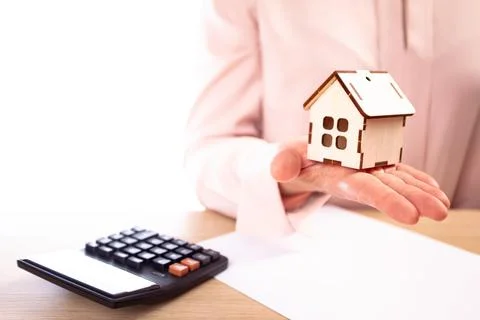 Woman holds model of house on hand, on the table lies a contract and calculator Stock Photos