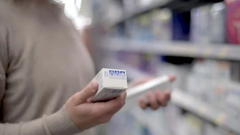 A woman holds two toothpaste boxes, comparing their details in a store aisle. Stock Footage 276398063