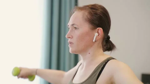 Woman at home performs exercises using dumbbells. The girl uses an application Stock Footage 166499571