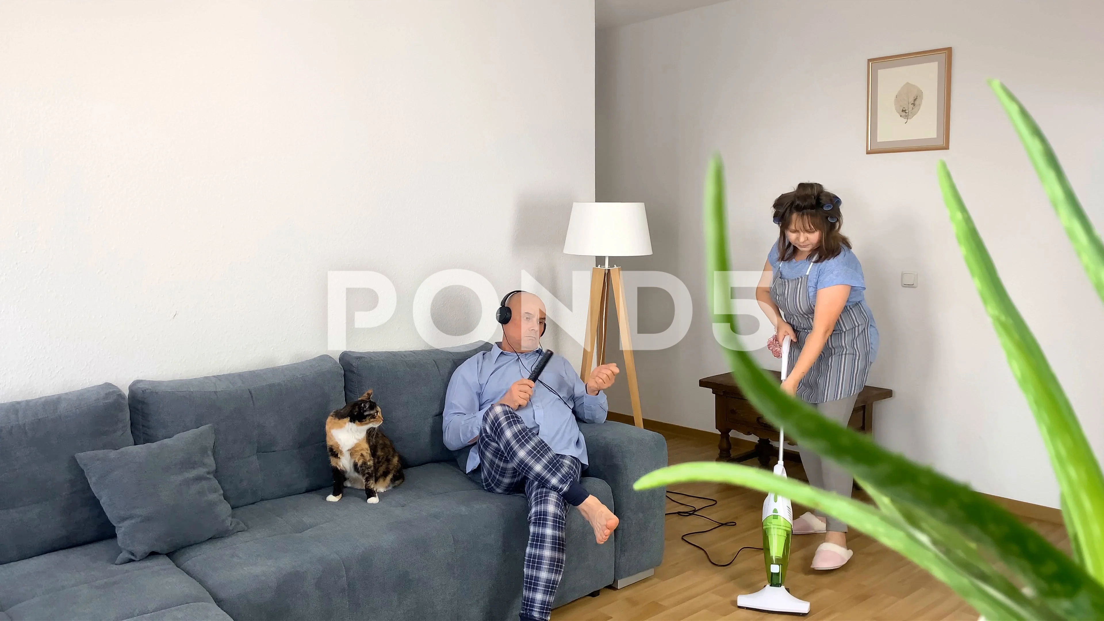 woman housewife in curlers, home clothes and apron vacuums the floors in