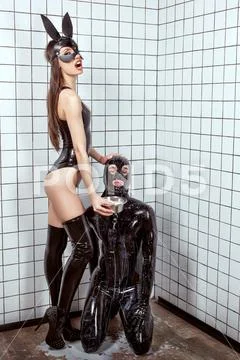 Woman humiliates a man in a latex suit. Stock Photos