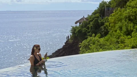 Woman in infinity pool drinking coffee and holding mobile phone. pretty sexy 스톡 동영상 123090272