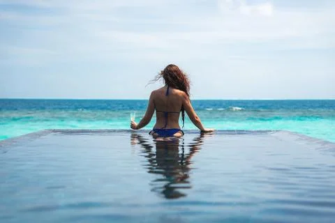 Woman at infinity pool facing turquoise ocean in the Maldives Stock Photos