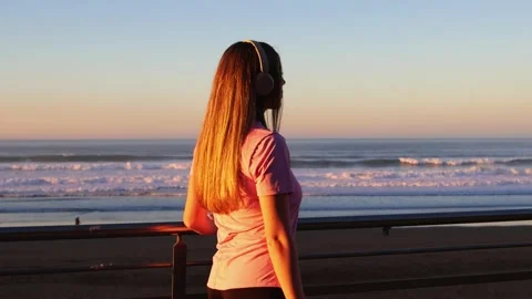 Woman inline skating along the beach at sunset listening to music Stock Footage 296557243