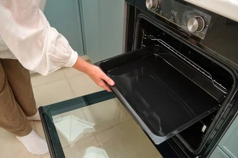 Woman inserting baking tray into modern electric oven in new kitchen. Female  Stock Photos