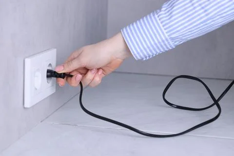Woman inserting electric plug into socket at white table indoors, closeup Stock Photos