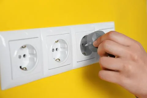 Woman inserting plug into power socket on yellow wall, closeup. Electrical .. Stock Photos
