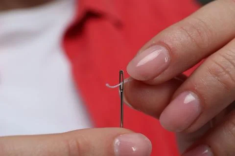 Woman inserting thread through eye of needle, closeup Foto stock