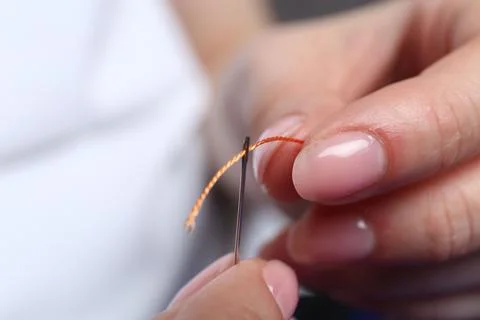 Woman inserting thread through eye of needle on blurred background, closeup Foto stock