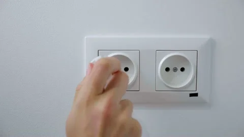 Woman Inserts plug Into electrical socket on a white wall Stock Footage 131880487