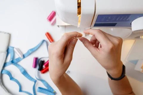 Woman inserts thread in sewing-machine Woman inserts thread in sewing mach... Foto stock