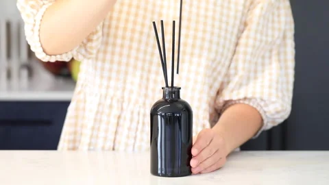 A woman inserts wooden sticks into a diffuser with a fragrance for the house. Video stock 241867012