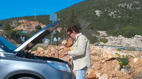 Woman inspecting broken car engine on roadside. Stock Footage 332718747