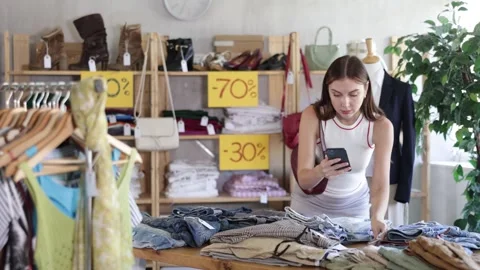 Woman with interest scans a QR code on a mobile phone in a clothing store Stock Footage 325034477