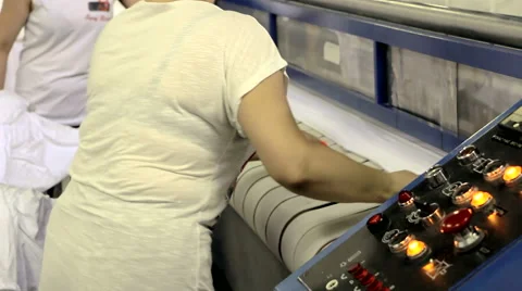 Woman ironed clean laundry on the industrial machine rolls Stock Footage