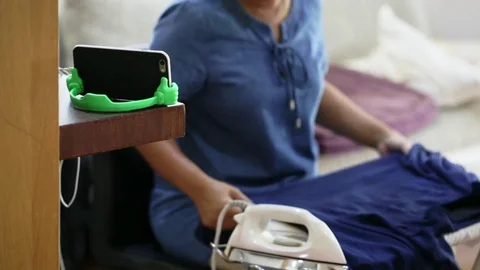 Woman ironing the cloth and watching content from smartphone Stock Footage