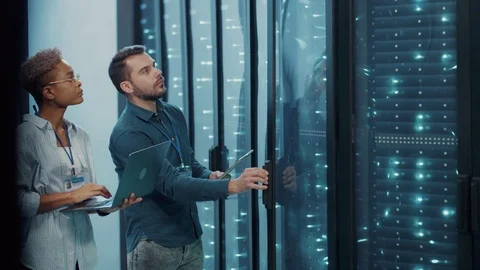 Woman IT administrator analyzing open server cabinet with tech specialist, doing Stock Footage 121224962