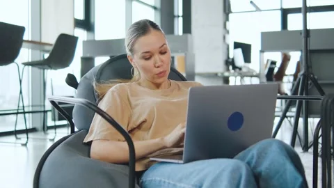 Woman IT works on laptop while sitting in modern office chair in a coworking Stock Footage 330690029
