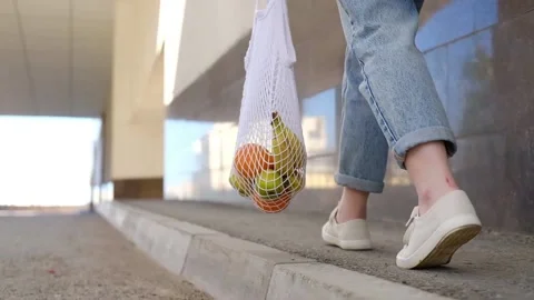 Woman in jeans walking and holding white mesh bag with fruits Stock Footage