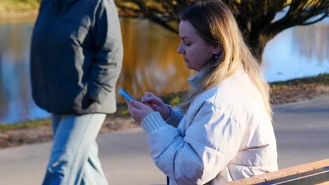 A woman is joyfully using her smartphone in a peaceful park by the water Stock Footage 307817182