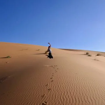 Woman jumping itn the air over sand dune in Sahara, Morocco, Africa Stock Photos