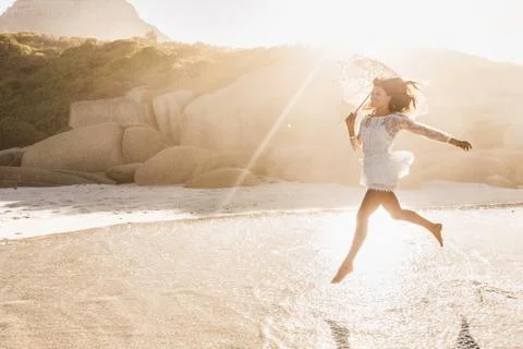 Woman jumping mid air with parasol on sunlit beach, Cape Town, South Africa Stock Photos