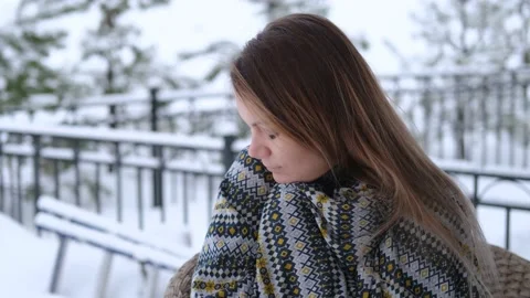 Woman keeps warm in a blanket while sitting in a chair on the street in winter Stock Footage 157181058