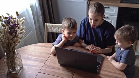 Woman with kids using computer. Caucasian mother assisting toddlers at kitchen Stock Footage 336972854