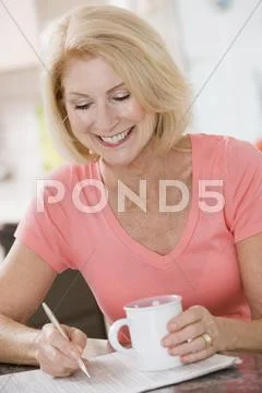 Woman in kitchen with coffee and newspaper smiling Stock-Fotos