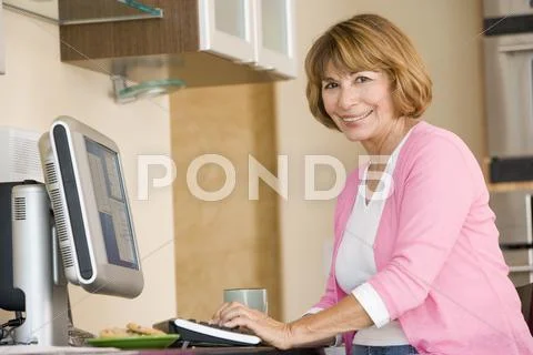 Woman in kitchen with computer and coffee smiling Stock-Fotos