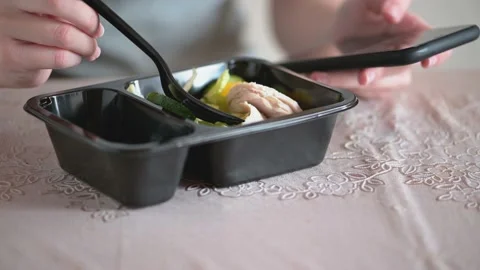 A woman in the kitchen eats salad from a plastic lunch box and looks at the Stock Footage 139442102