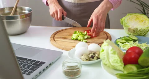 A woman at the kitchen table prepares a vegetable salad according to the recipe  Stock Footage 153096978