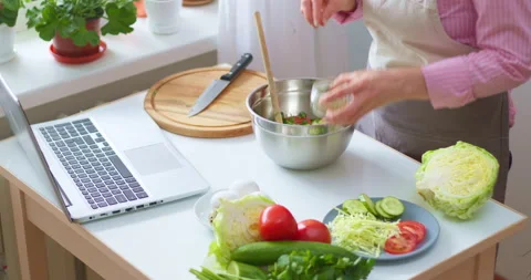 A woman at the kitchen table prepares a vegetable salad according to the recipe  Stock Footage 153097675