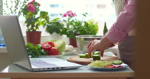 A woman at the kitchen table prepares a vegetable salad according to the recipe  Stock Footage 153097682