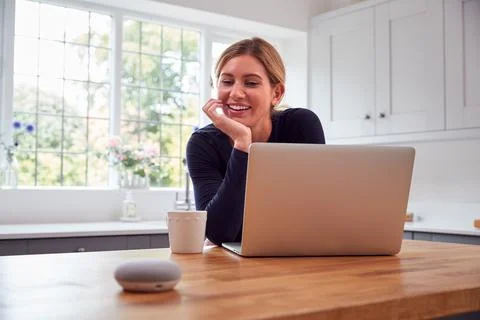 Woman In Kitchen Using Digital Smart Speaker Whilst Working From Home With Foto stock