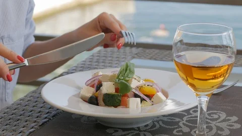 A woman with a knife and fork eats a beautiful Greek salad in a restaurant on Stock Footage 119620175