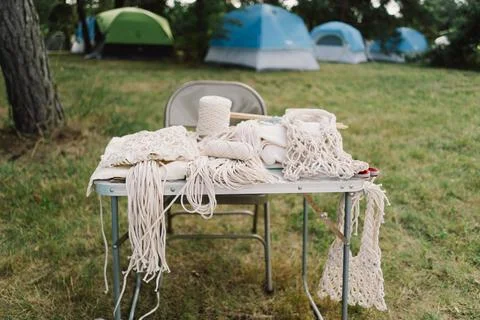 Woman knits bag using macrame technique outdoors near tents. Outdoor hobbies. Stock Photos