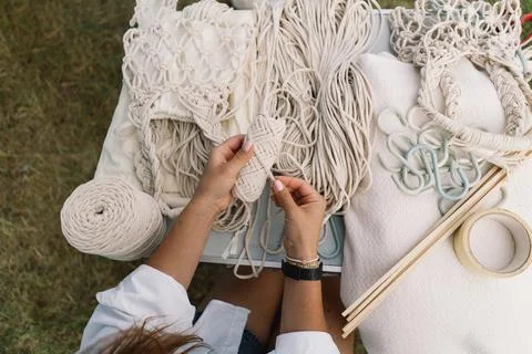 Woman knits bag using macrame technique outdoors near tents. Outdoor hobbies. Stock Photos
