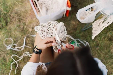 Woman knits bag using macrame technique outdoors near tents. Outdoor hobbies. Stock Photos