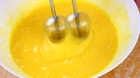 Woman knocks broken eggs in a large white deep dish with a mixer on a wooden Stock Footage 145960050