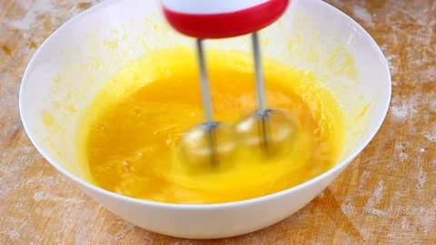 Woman knocks broken eggs in a large white deep dish with a mixer on a wooden Stock Footage 148006753