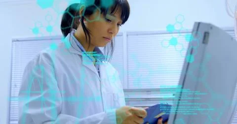 Woman in lab coat analyzing data on monitor at research lab, with clipboard and Foto stock