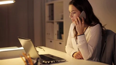 Woman with laptop calling on smartphone at office Stock Footage